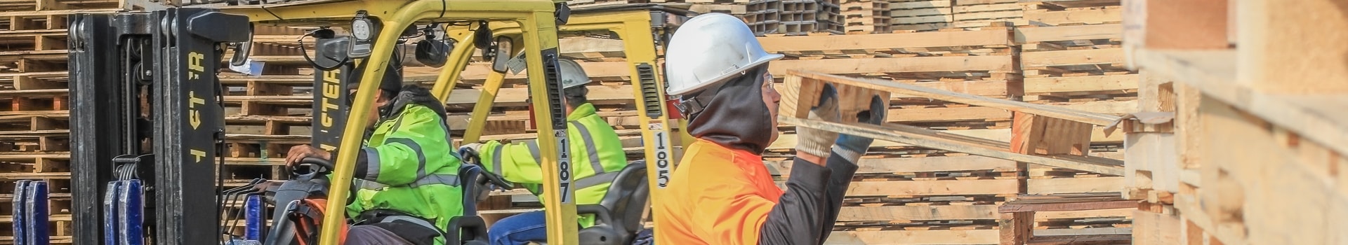 Man wearing white hard-hat lifting used wooden pallet