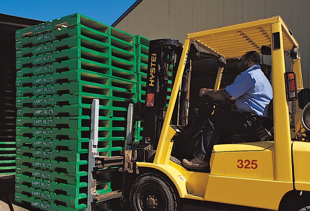 Kamps employee moving green pallets with a forklift