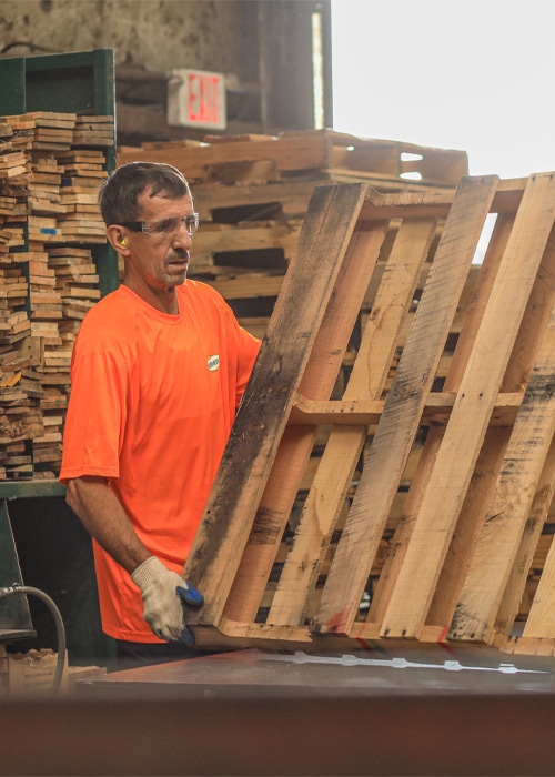 Kamps employee in orange shirt repairing a wooden pallet