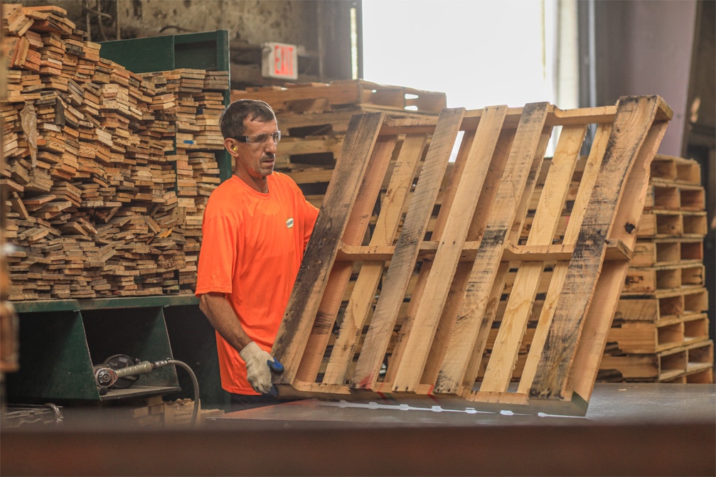 Kamps employee wearing an orange safety shirt inspecting a pallet for repair