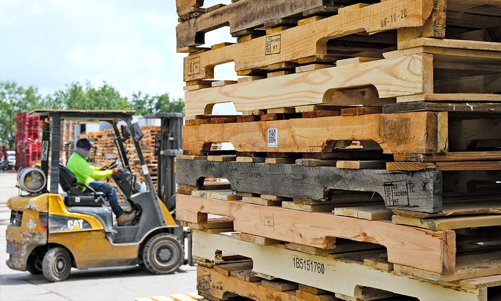 Kamps employee driving forklift by stacks of pallets