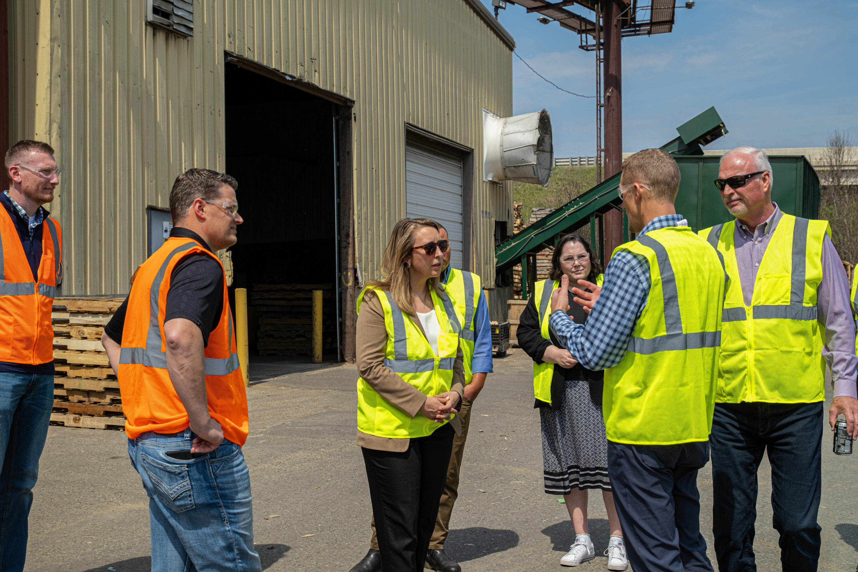 A group of men and women wearing high visibility vests walking in pallet yard.