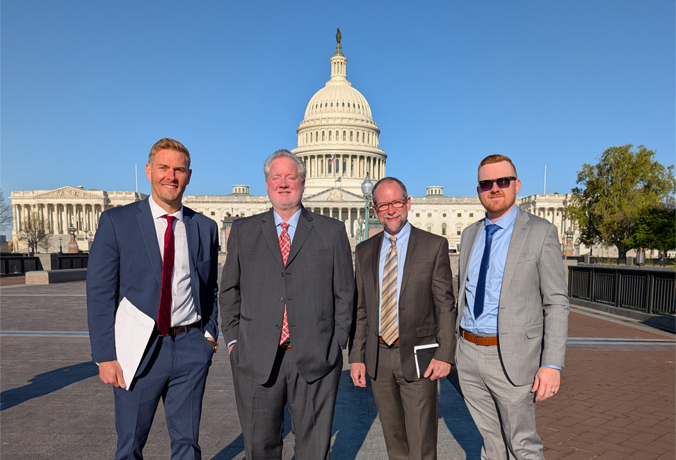 Four middle-aged men in suits standing in front of the United States Capitol building