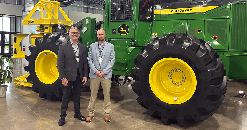 Damon and Rob Two professional men standing in front of large green tractor indoors